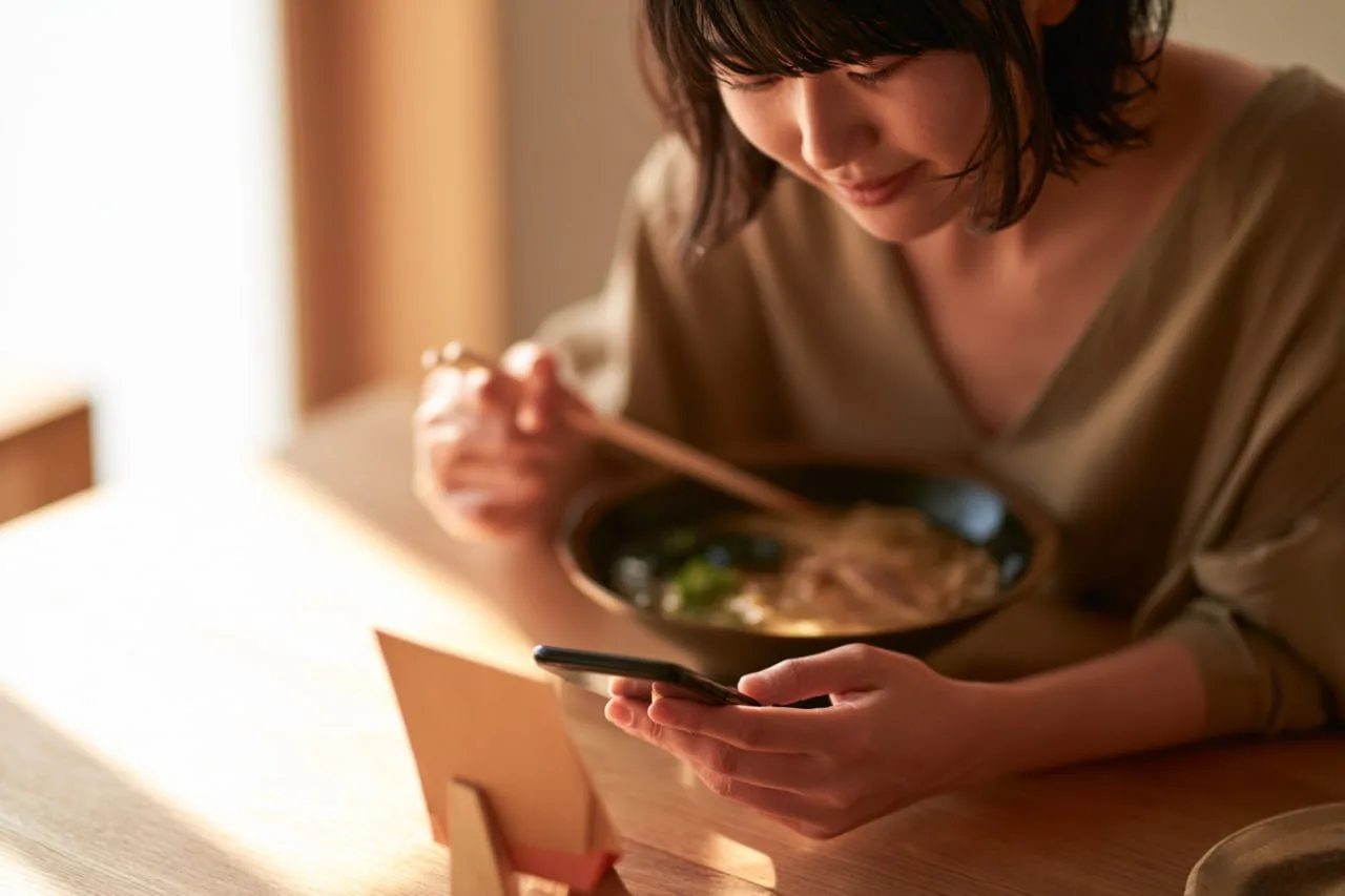 テーブルのカードを見ながらスマートフォンで注文する女性